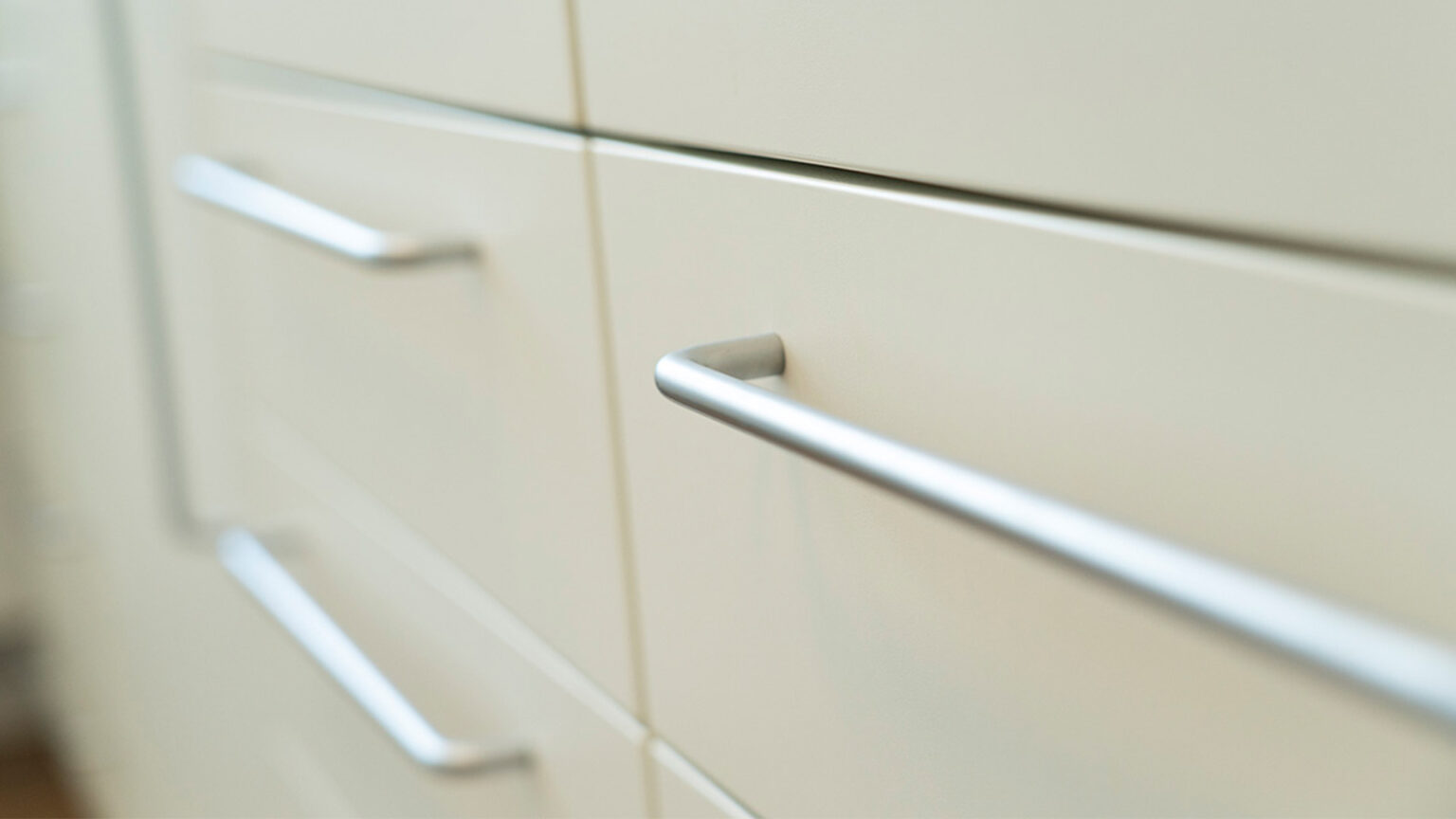 Detailaufnahme von hellen Schrankfronten mit schlichten, gebürsteten Edelstahlgriffen in einer Zahnarztpraxis.