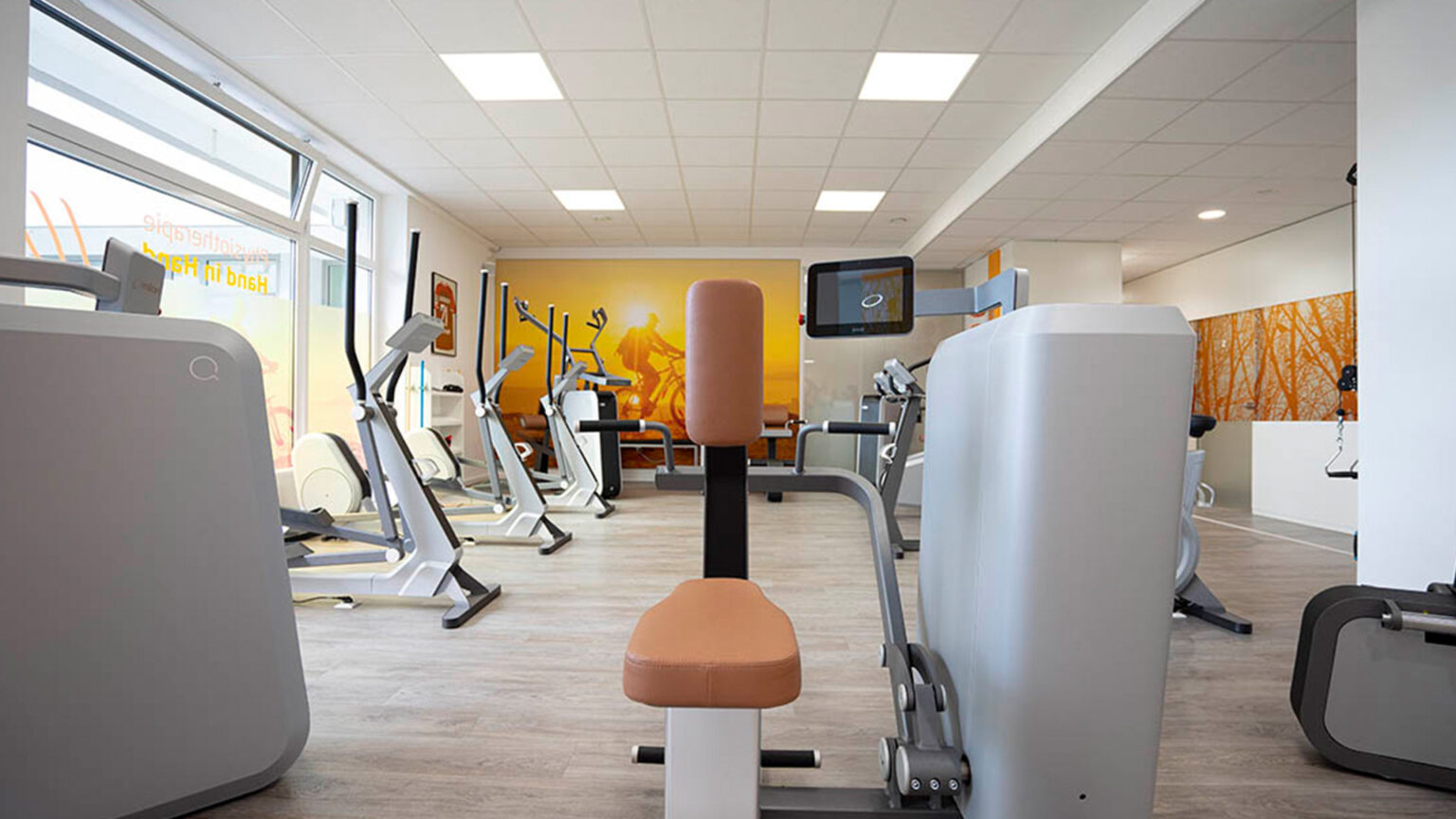 Moderner Fitnessraum mit Trainingsgeräten und warmer, heller Atmosphäre.