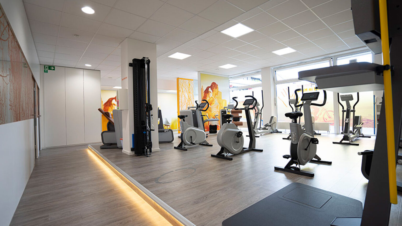 Moderner Fitnessraum mit Trainingsgeräten und warmer, heller Atmosphäre.